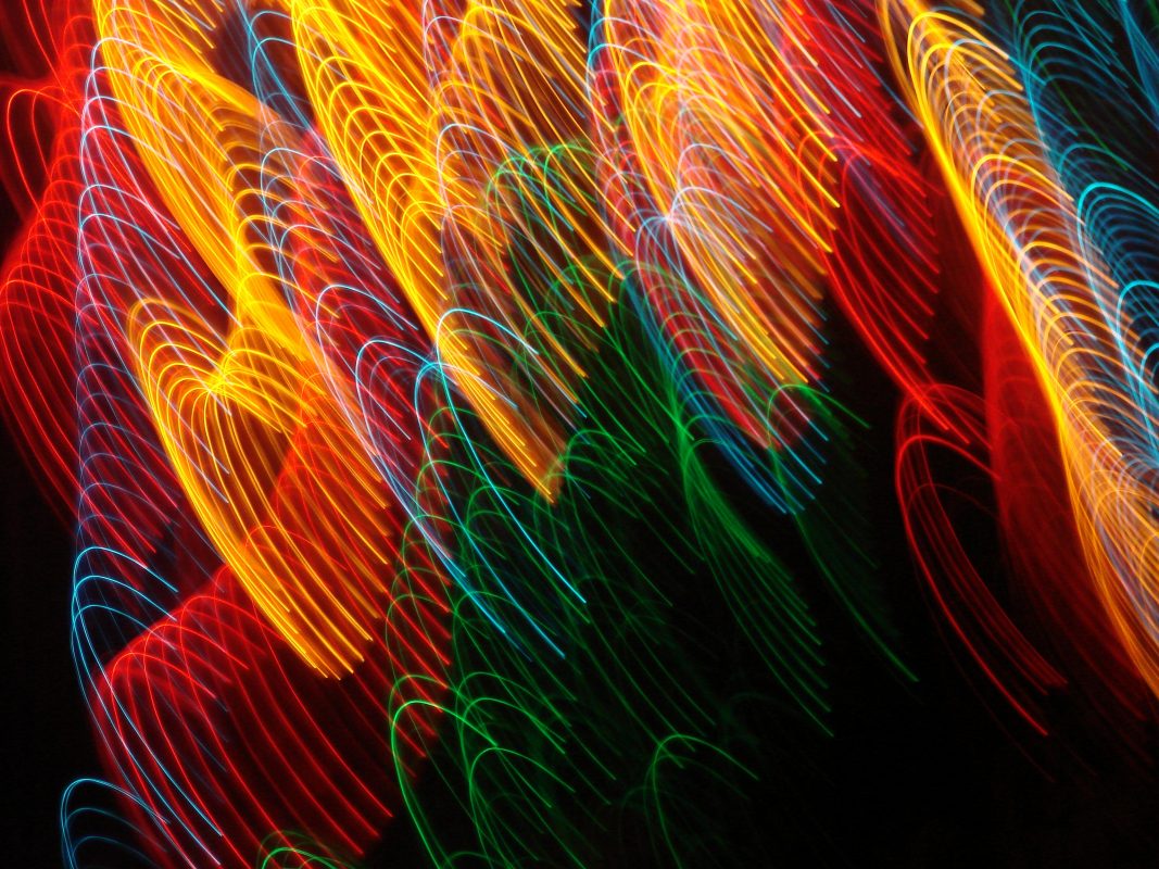 A vibrant abstract image featuring swirling patterns of light in red, yellow, green, and blue against a dark background, creating a dynamic and energetic visual effect.
