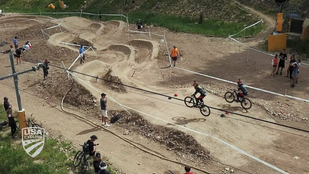 Overview of the intermediate slopestyle track with racers in each lane and spectators on the side of the course