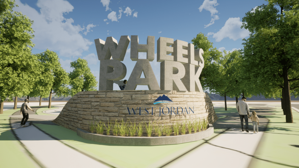 The image shows a stone structure with large metal letters spelling Wheels Park on top. Below, West Jordan is written with a blue mountain logo. Trees surround the area, and people walk nearby under a clear blue sky.