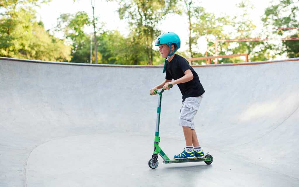 Young boy rides his scooter in a skate bowl