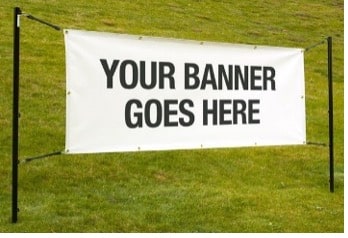 A white banner with the text YOUR BANNER GOES HERE stands on a grassy lawn, supported by a simple black frame.