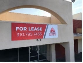 A commercial building with a large For Lease banner hangs over the entrance. The sign includes a contact phone number and the logo of Global Commercial in red and white.